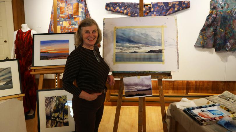 Woman stands in front of a selection of paintings.