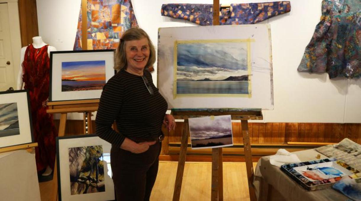 Woman stands in front of a selection of paintings.